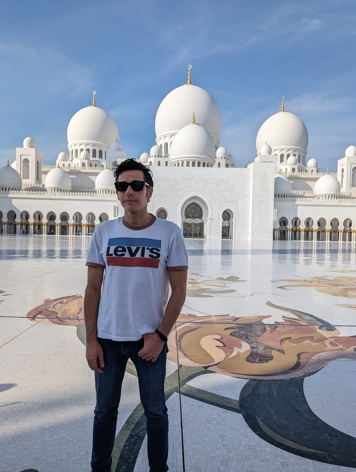 The full marble facade and courtyard of Sheikh Zayed Grand Mosque, with visitors on the mosaic floor