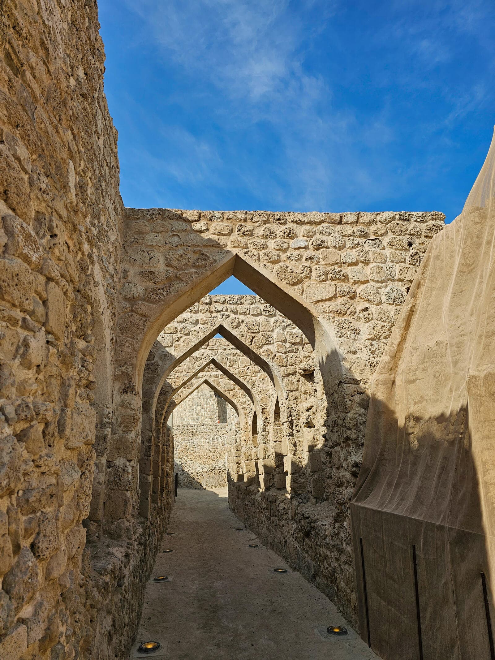 A stone archway corridor inside Bahrain Fort, with a sequence of arches leading toward the main structure