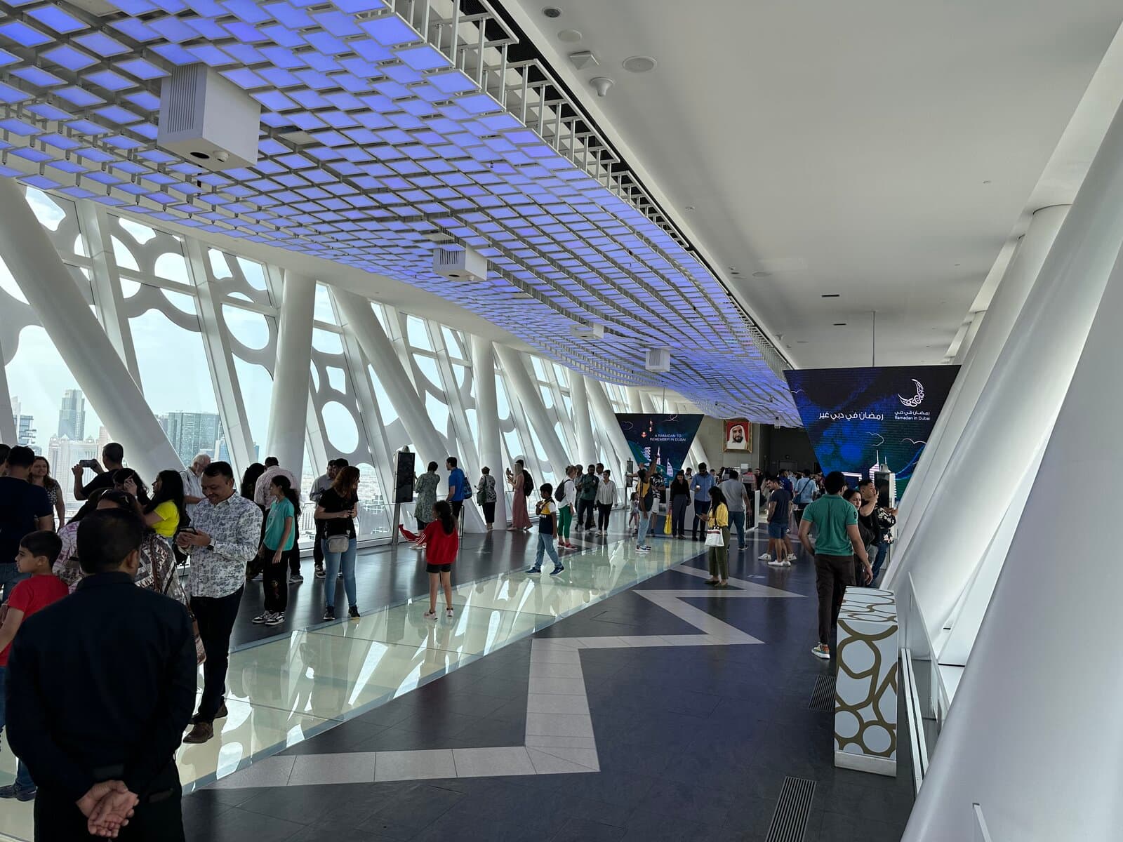 Visitors on the glass-floored walkway inside the Dubai Frame observation deck, with the Dubai skyline visible through the angled white columns