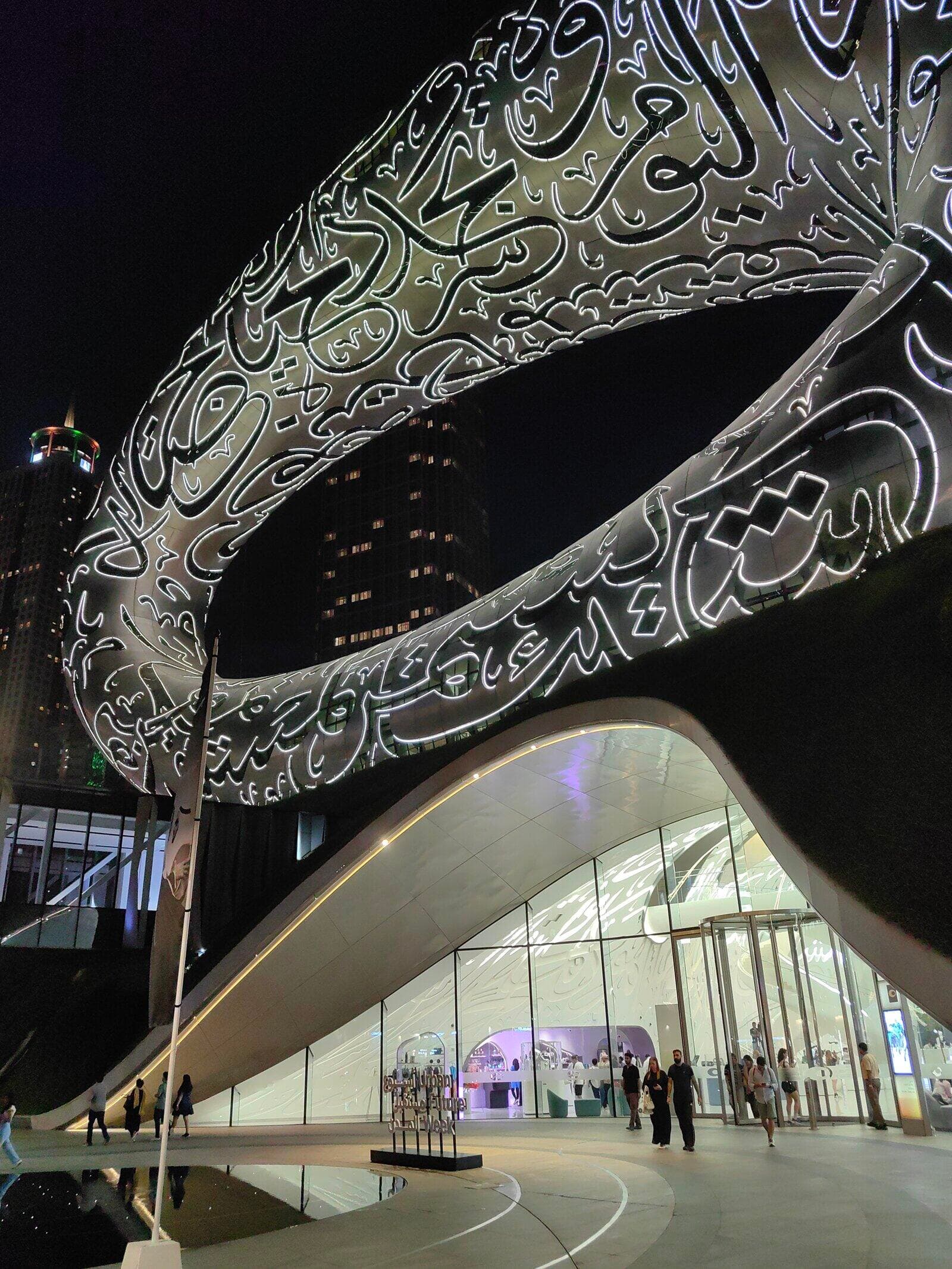 The Museum of the Future's torus-shaped exterior lit up at night, with Arabic calligraphy across its facade