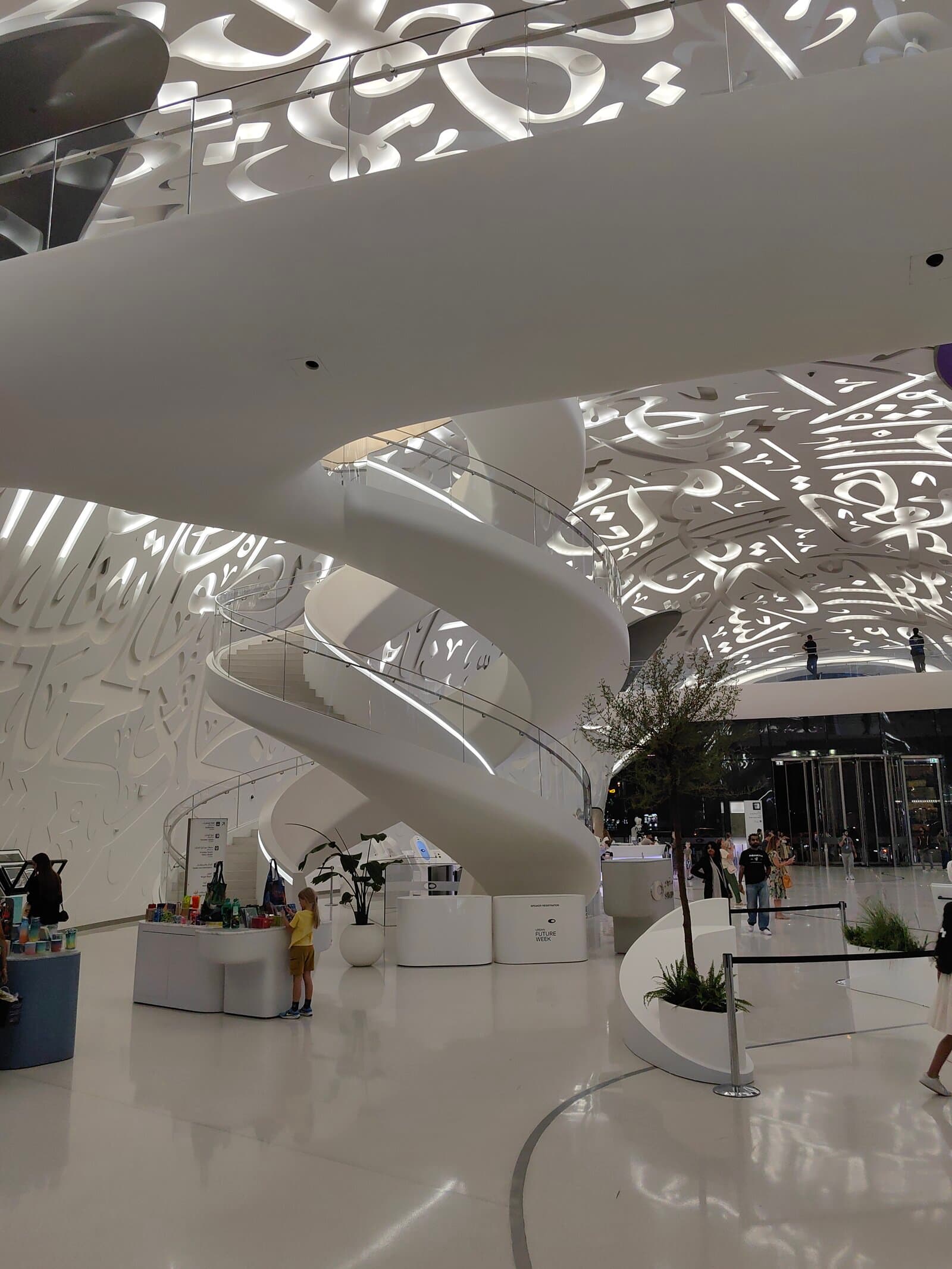 The Museum of the Future's spiral staircase and calligraphy ceiling in the lobby, with a small retail kiosk visible below